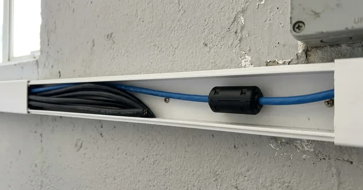Blue communication cable with clip-on ferrite bead routed in wall trunking alongside black power cables. — SolarNevs spec card